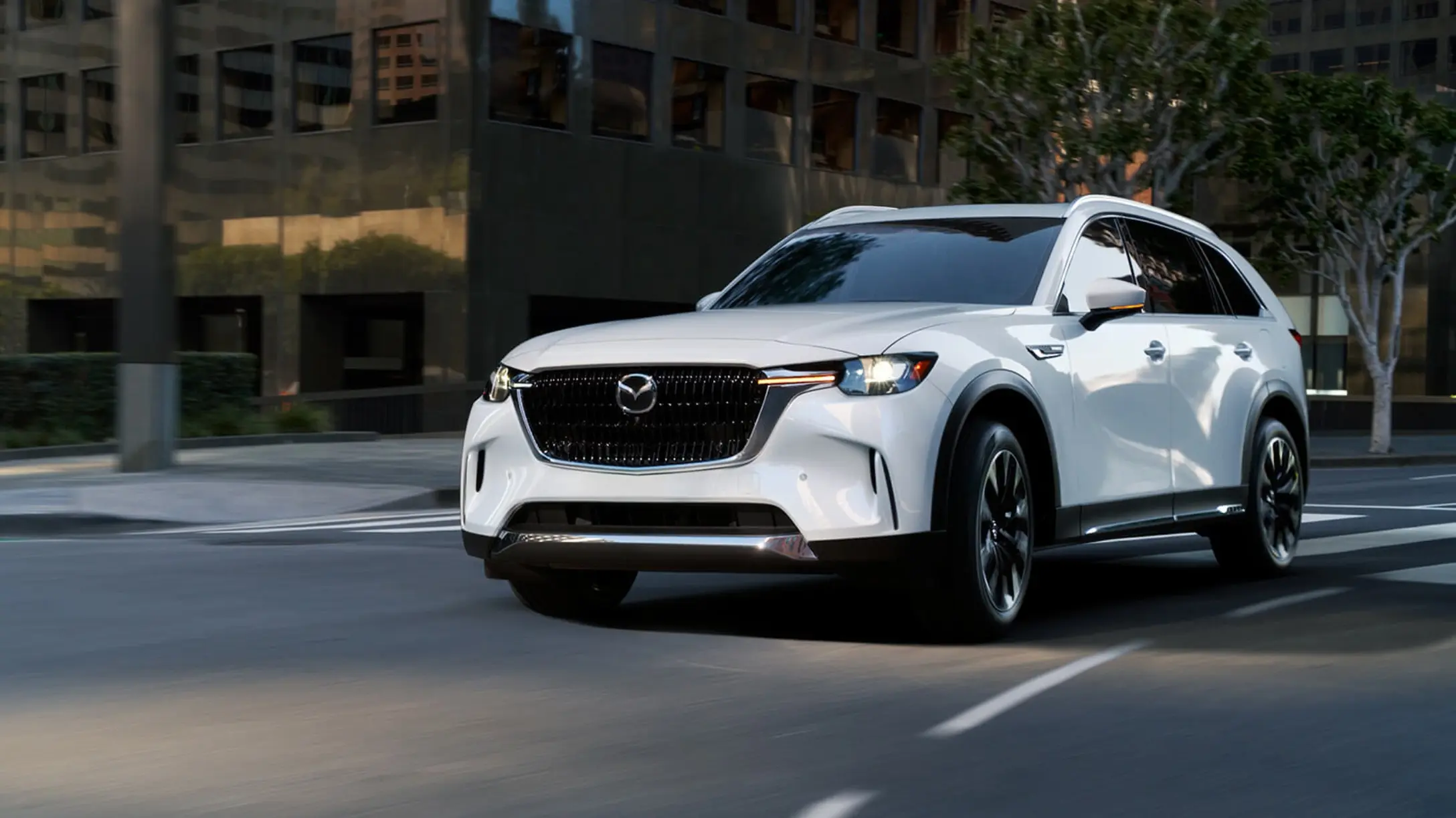 Mazda CX-90 blanco en movimiento, desplazándose por una calle urbana.