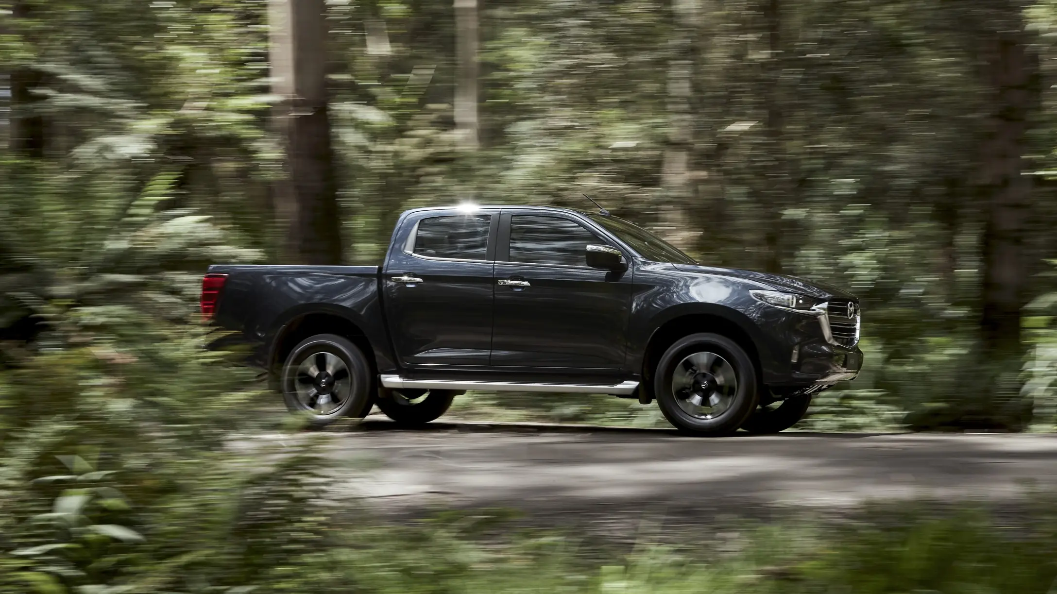 Mazda BT-50 negra en movimiento en un entorno boscoso.