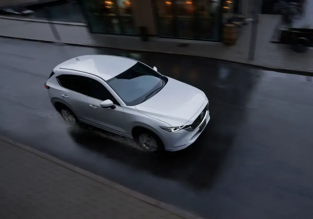 Mazda circulando en lluvia intensa en ciudad (parabrisas con gotas, entorno urbano visible).
