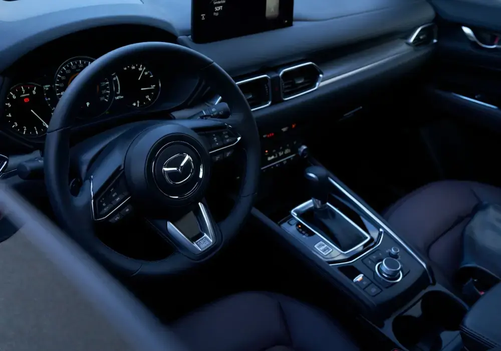 Conductor manejando un Mazda CX-5  (interior), con volante y panel visibles en entorno urbano.
